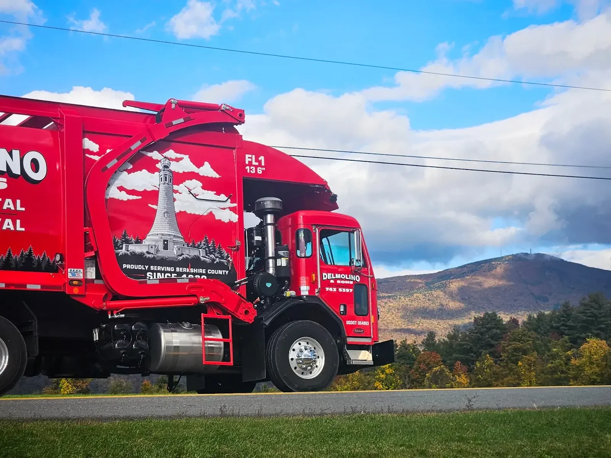 Red Delmolino & Sons front-load collection truck with its mountain monument design and Berkshire hills behind it