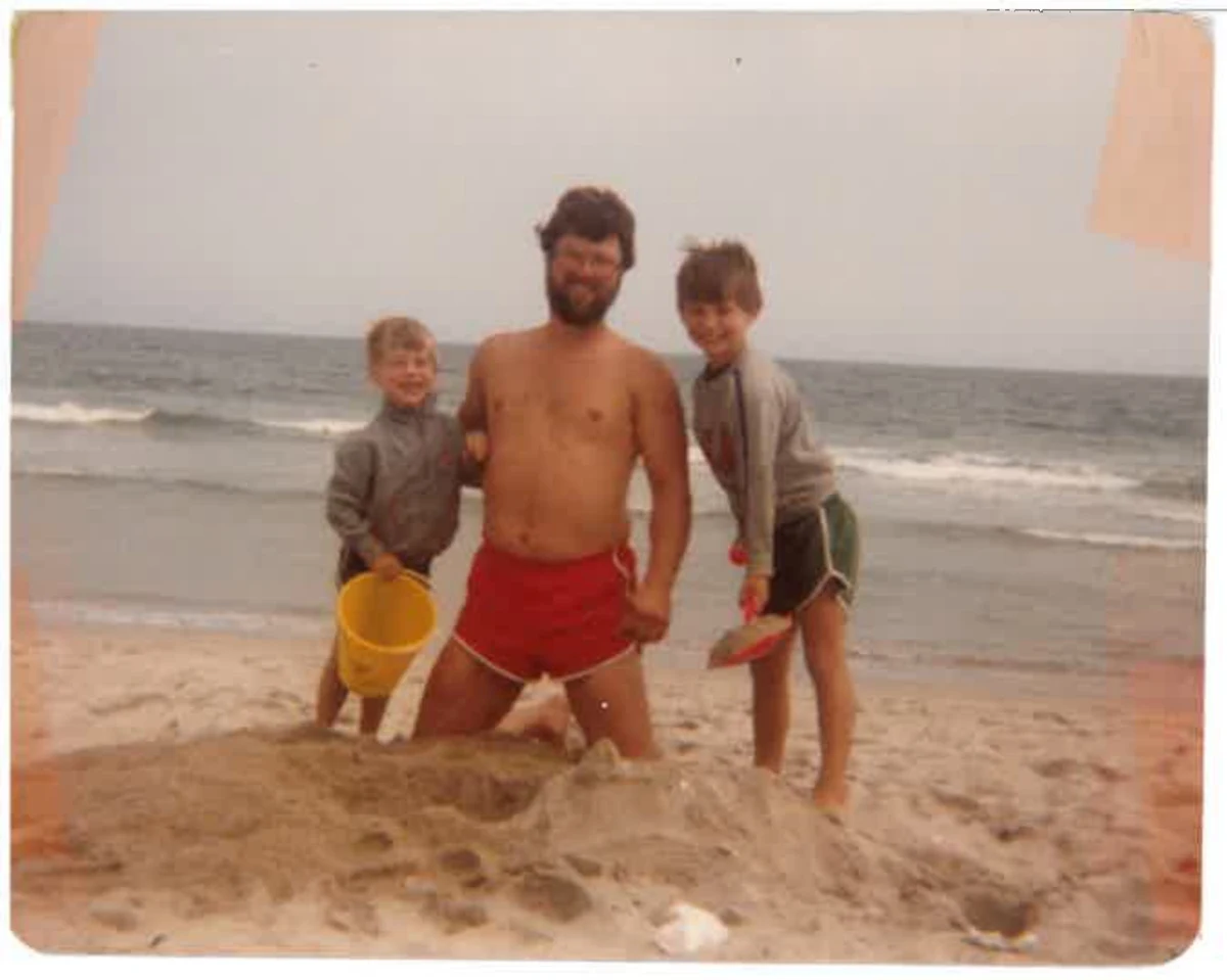 An adult and two children building a sandcastle at the beach