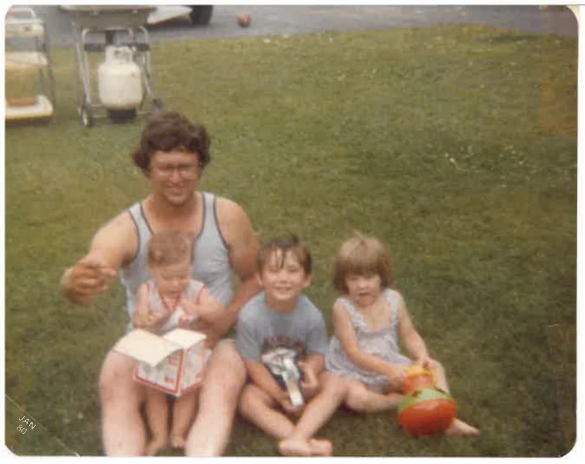 An older family photograph of an adult and three children seated together on a lawn