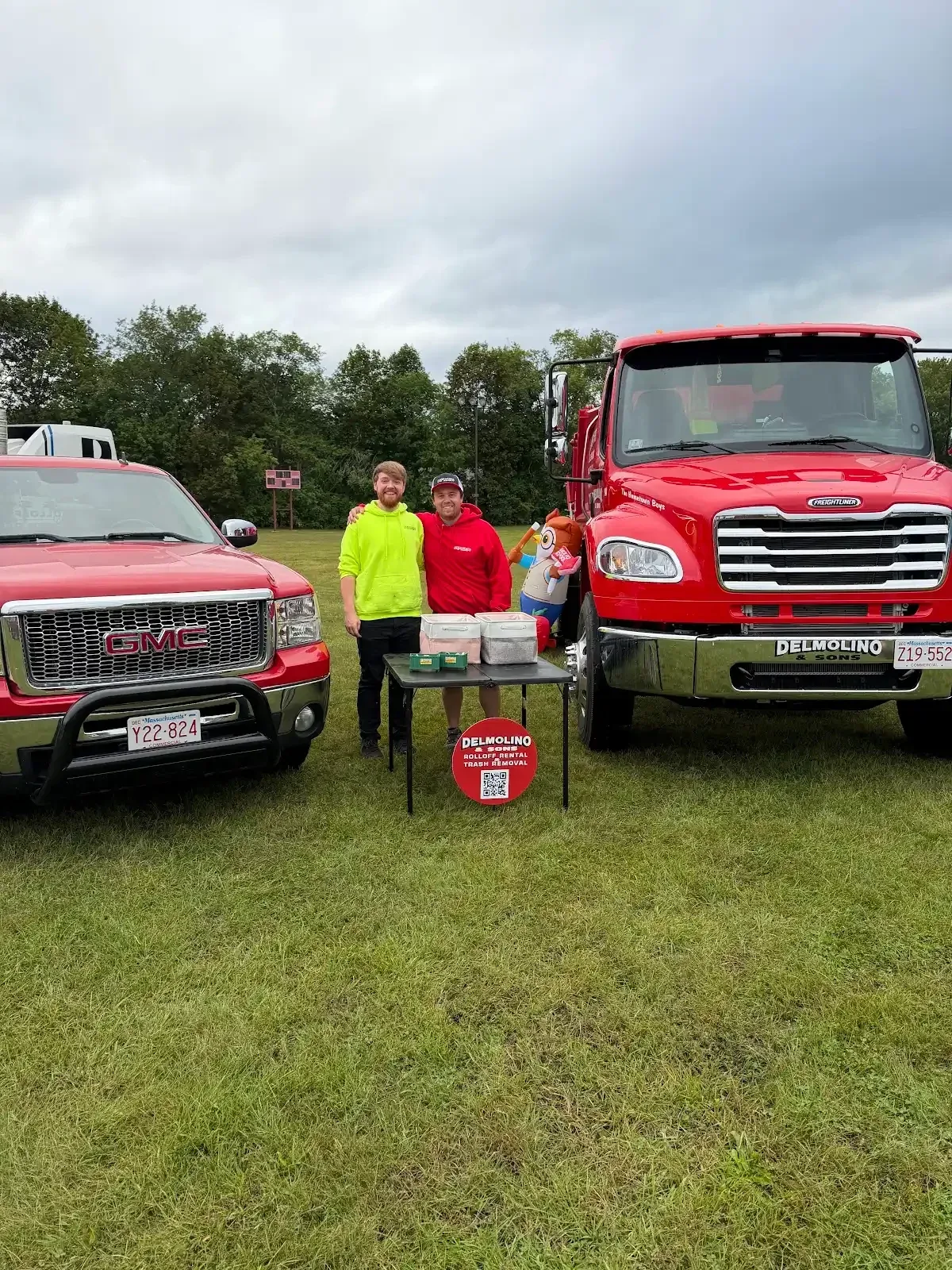People gathered beside Delmolino & Sons vehicles at an outdoor event