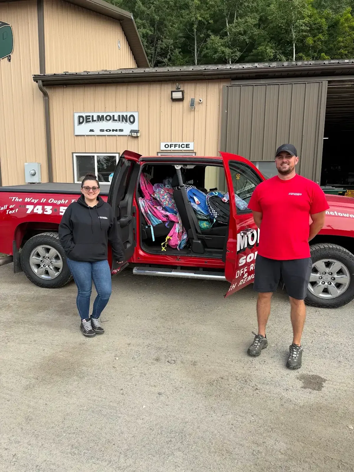 Two people beside a Delmolino & Sons pickup with backpacks outside the office