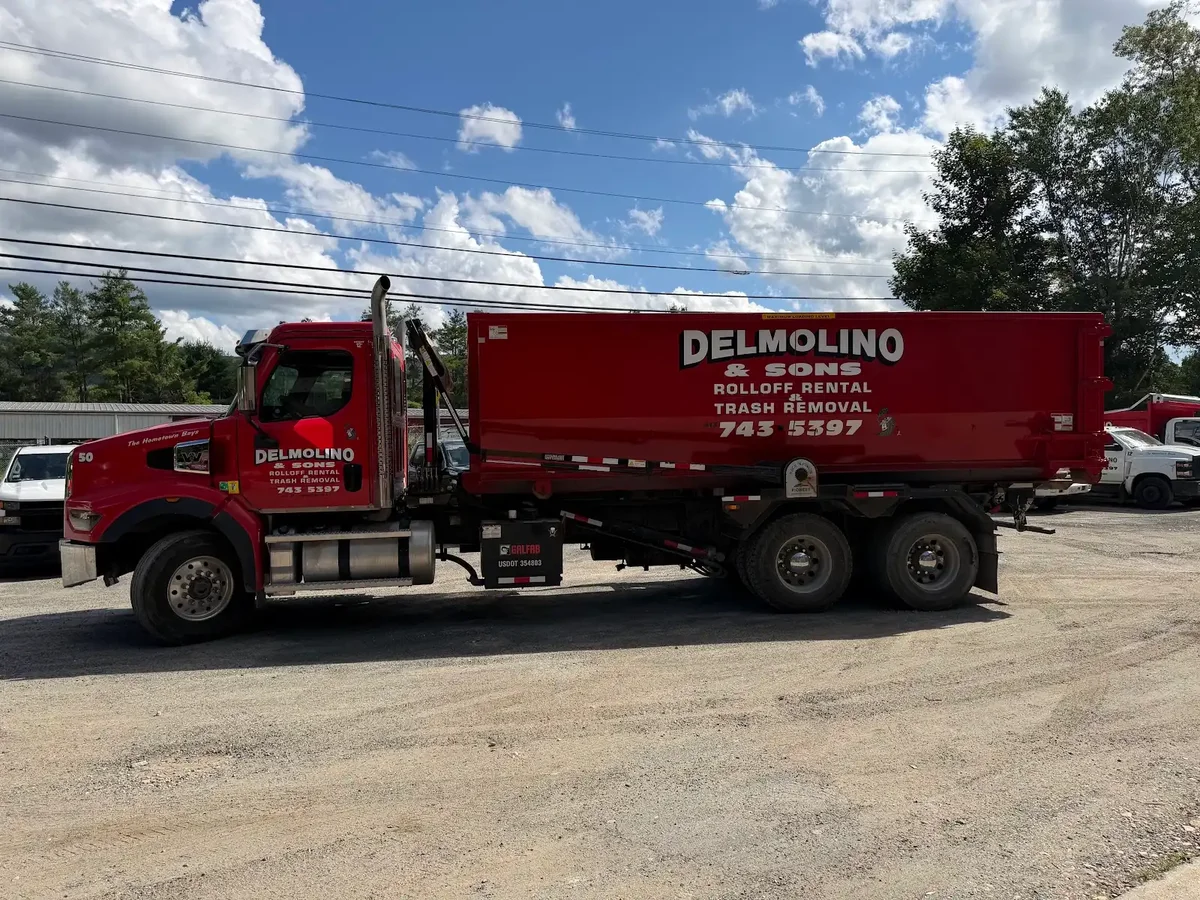 Red tub-style Delmolino & Sons roll-off dumpster with a large company decal loaded on a red truck